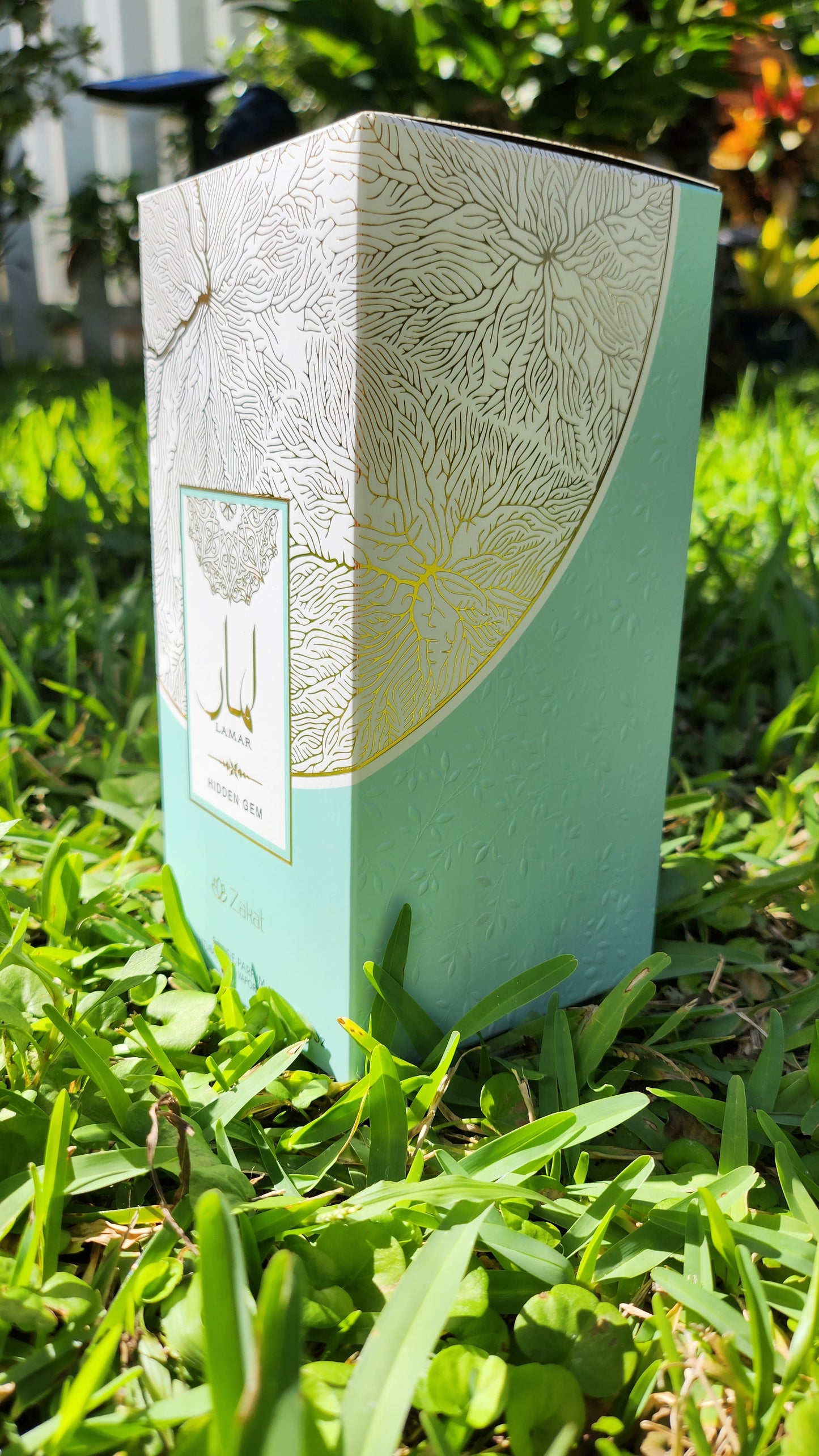 Lamar Hidden Gem by Zakat Perfume Box standing over a grass field picture taken from the side of the box.